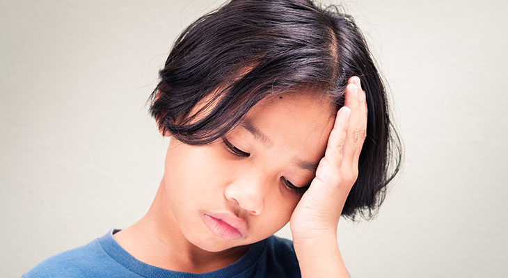 A child holds his head in pain, illustrating possible symptoms of a headache or migraine.
