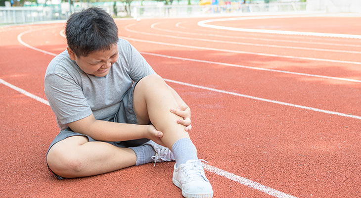 A child grabs their leg while wincing in pain, indicating a common sign of sports overuse injuries in children.